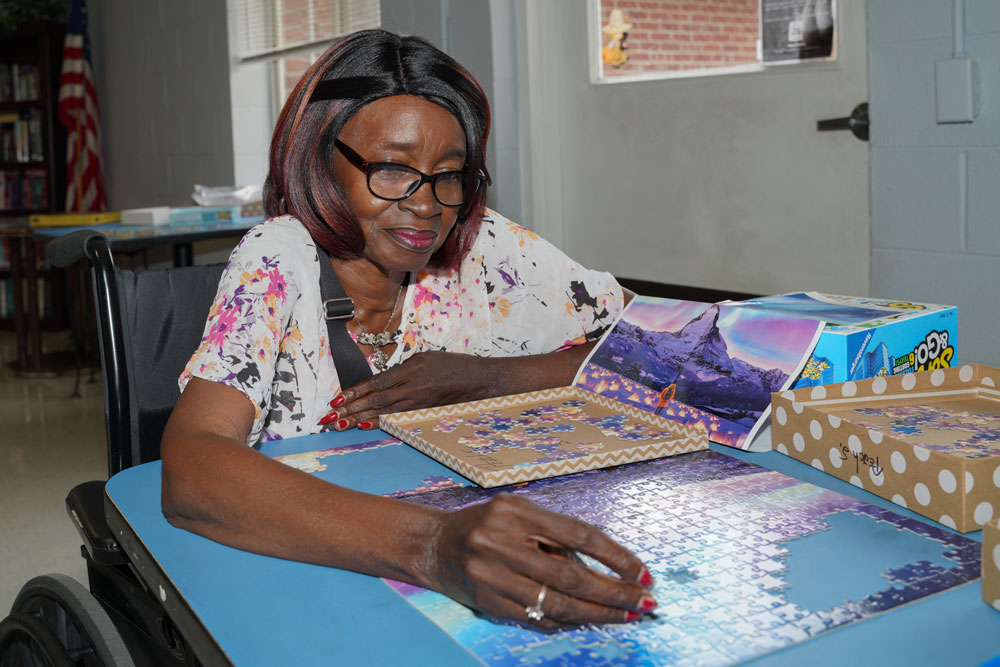 A senior African American woman sitting at a table placing a puzzle piece