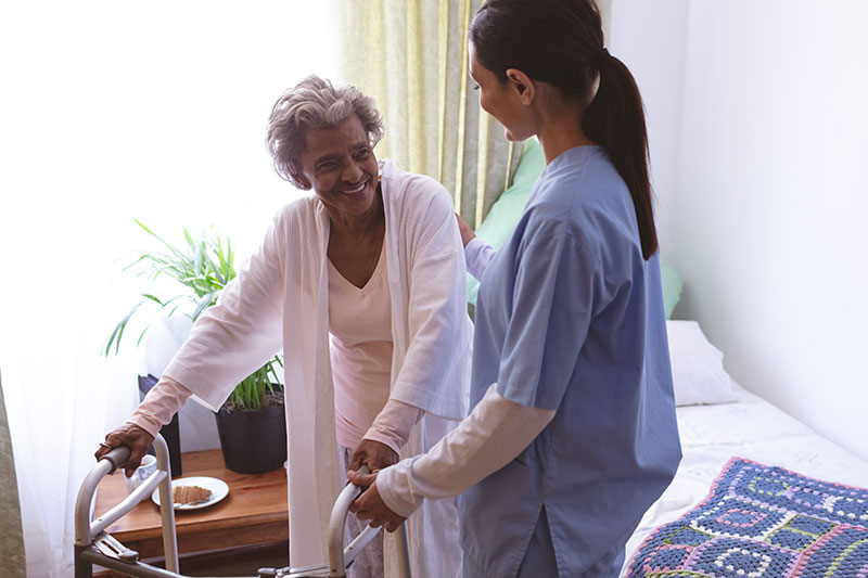 An older African American woman being helped out of bed by a skilled nurse